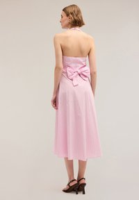 Rochie midi roz în dungi, cu gât halter și talie strânsă, având un detaliu mare sub formă de fundă la spate. Țesătură netedă cu o siluetă fluidă.