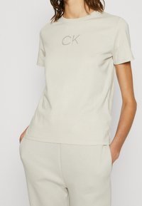 T-shirt in cotone beige con maniche corte, caratterizzato da un logo CK discreto al centro. Collo rotondo classico e vestibilità rilassata.