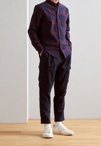 Camicia a maniche lunghe a quadri rossi e blu con colletto button-down, abbinata a pantaloni cargo neri e sneakers bianche con un design testurizzato.