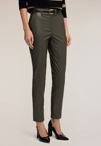 Olivekowe spodnie z ekologicznej skóry o prostym kroju, z czarnym spodniem wysadzanym ćwiekami, zestawione z czarnymi, lakierowanymi szpilkami.