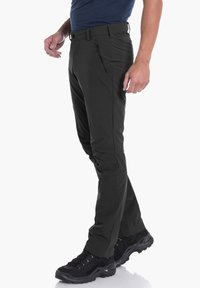 Schwarze, schmal geschnittene Wanderhosen mit glatter Textur, ausgestattet mit einer Fronttasche mit Reißverschluss und Gürtelschlaufen, kombiniert mit robusten schwarzen Wanderschuhen.