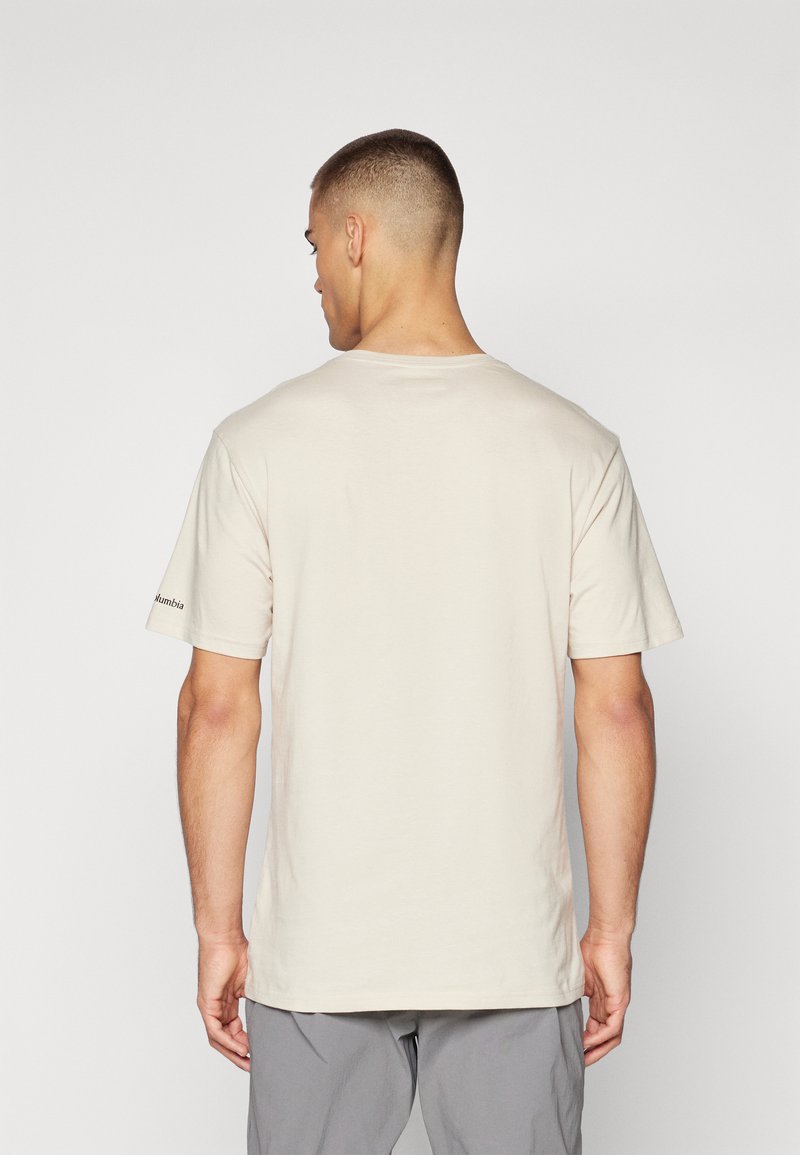 T-shirt beige a maniche corte con colletto rotondo, texture liscia e dettaglio logo nero sulla manica sinistra. La vista posteriore mostra una vestibilità rilassata.