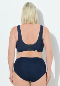 Marineblauw bh en hoge slipset met een stippenpatroon, brede bandjes en een haak-en-oogsluiting op de rug.