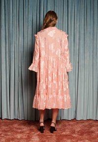 Ružové midi šaty s kvetinovým vzorom, zdobené volánikovými rukávmi a vrstvenou sukňou. Vyrobené z textúrovaného materiálu s vyšívanými kvetmi, majú voľný strih.