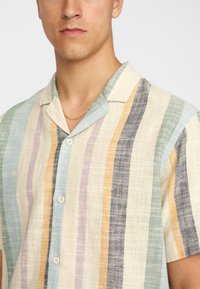 Short-sleeve button-up shirt made of light fabric, featuring horizontal stripes in green, blue, purple, yellow, and navy on a beige base.