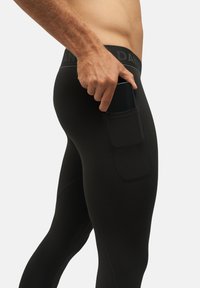 Leggings de sport noirs à texture lisse comportant une poche latérale contenant un smartphone. La ceinture porte un logo de la marque.