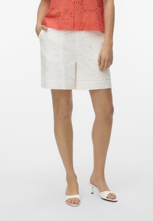 Witte shorts met bloemenborduursel, net boven de knie geknipt. Combinatie met witte haksandalen. Achtergrond is eenvoudig en neutraal.