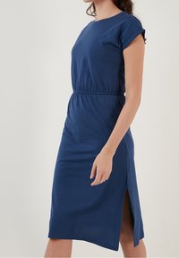 Robe en coton bleu marine, manches courtes, taille élastique, longueur au genou avec fente sur le côté. Design simple avec une texture lisse et un col rond classique.