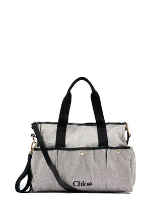 Borsa Chloé in tessuto beige con manici neri, tasche frontali e tracolla nera regolabile su sfondo bianco.