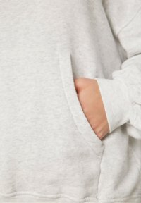 Sudadera gris claro con un bolsillo tipo canguro, puños acanalados y textura de felpa suave. La tela parece acogedora y informal.
