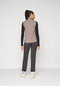 Lichte, mouwloze taupe vest met een gestructureerd ontwerp. G dragen over een zwart longsleeve shirt en gecombineerd met donkere broeken en beige schoenen.