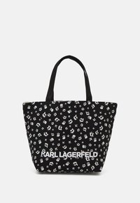 Sac fourre-tout en tissu noir avec un motif répété de lunettes de soleil et de lettres en blanc et gris. Dispose de poignées noires robustes et d'un logo blanc.