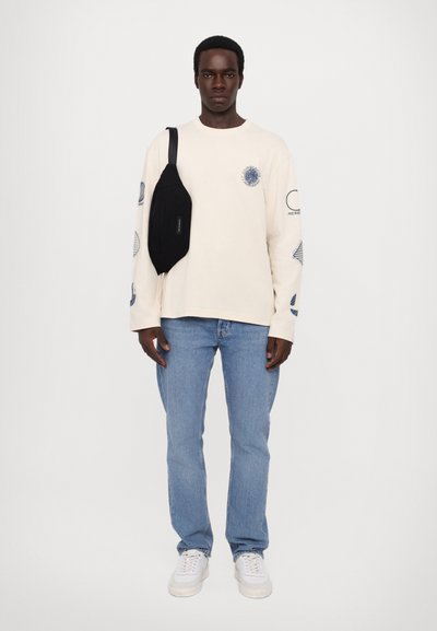 Long-sleeve cream shirt with blue graphic prints, paired with light blue jeans and white sneakers, complemented by a black crossbody bag.