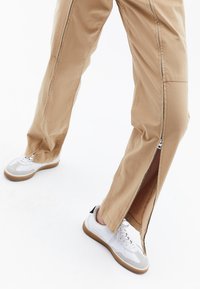Lichtbeige cargobroek met zijritsen, met een rechte pijpdesign. Gepaard met witte sneakers met grijze accenten en rubberen zolen.