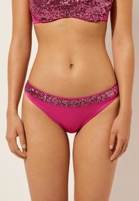 Rosa bikiniunderdelar med en blank texturerad midjeband prydd med paljetter. Tyget är slätt och i en enhetlig rosa färg.