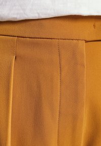 Senapsgula byxor med en mjuk textur, framfickor och synliga sömmar längs sömmarna för en strukturerad detalj.