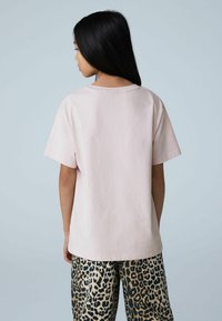 T-shirt en coton rose clair à coupe décontractée, manches courtes et encolure arrondie. Associé à un pantalon imprimé léopard avec des tons noirs et dorés.