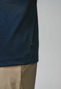 Marineblå, svedtransporterende athletic shirt med et struktureret geometrisk mønster, detaljeret kant og et lille mærketag; parret med lyse khaki bukser.