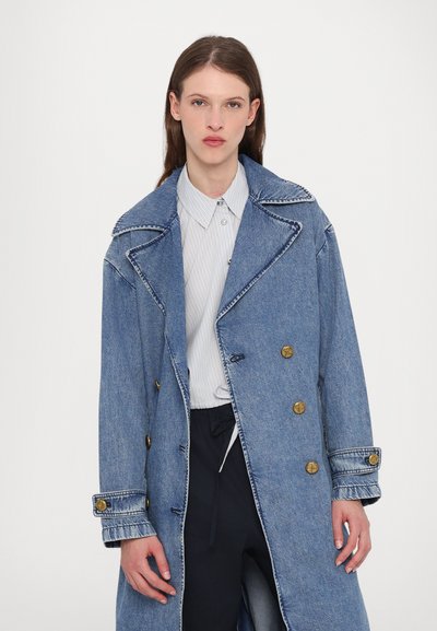 Sinine teksariidest kahekordne trench coat, millel on silmapaistev krae, kuldse tooni nupud ja nähtavad õmblusdetailid. Kandes triibulise särgi peale.