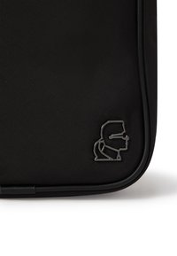 Borsa in tessuto nero con superficie testurizzata, angoli arrotondati e un logo metallico sulla parte anteriore. Chiusura con zip lungo il bordo.
