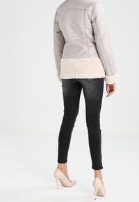 Chaqueta acolchada gris claro con un suave borde de piel crema en el dobladillo y los puños, combinada con jeans ajustados oscuros y tacones altos claros.