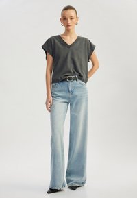 Grijze katoenen V-hals t-shirt met korte mouwen, gecombineerd met lichtblauwe wide-leg jeans met een hoge taille en een zwarte riem.