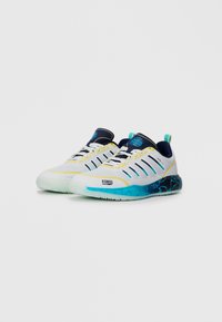 Chaussures de sport pour hommes en blanc et marine avec des accents jaunes, présentant une tige texturée, plusieurs rayures de ventilation et une semelle dégradée bleue.