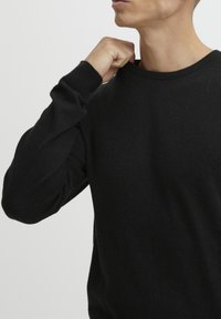Fekete kötött pulóver kerek nyakkivágással. Hosszú ujjú, bordás mandzsettával. Az anyag lágy, enyhe textúrával rendelkezik.