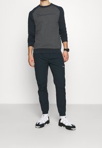 Tummanharmaa collegepaita laivastonsinisillä raglanhihoilla, siihen sopivat tummat verkkarit logolla ja urheilulliset valkoiset kengät mustilla yksityiskohdilla.