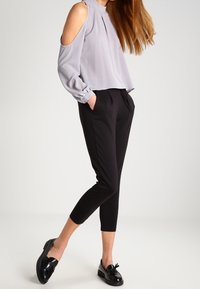 Blouse gris clair à épaules dénudées avec plis, associée à un pantalon noir raccourci et des mocassins noirs. Tissu lisse, coupe décontractée.