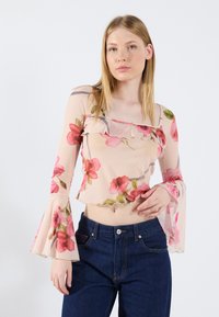 Haut floral léger et transparent avec des motifs de roses roses et vertes, manches cloche et ourlet en dentelle, associé à un jean en denim foncé.