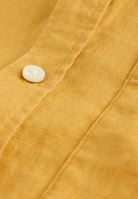 Tissu jaune avec un tissage texturé et un bouton blanc cousu près d'une couture.