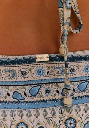 Close-up of patterned blue and white bikini bottom with floral designs and tied strings on tanned skin.