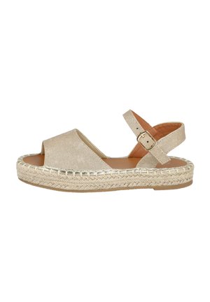 Sandal de esparto de tela dorada con punta abierta, correas entrecruzadas, hebilla en el tobillo y detalles de suela de cuerda trenzada. Diseño de tacón plano.