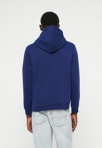 Un sweat à capuche bleu marine avec cordon de serrage, à coupe décontractée, avec des poignets et un ourlet côtelés, porté par-dessus un jean en denim clair.