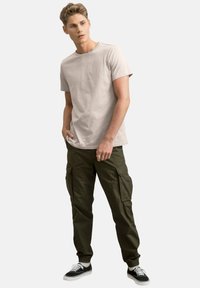 T-shirt a maniche corte grigio chiaro abbinato a pantaloni cargo verde oliva con molteplici tasche e polsini elastici. Sneakers nere con dettagli bianchi.