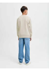 Sudadera beige de manga larga, con cuello redondo y puños acanalados, combinada con jeans sueltos de color azul claro y zapatillas blancas.
