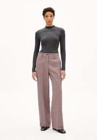 Grijze ribgebreide coltrui gecombineerd met roze wijde broek met knoopsluiting. Zwarte schoenen met zilveren studs maken de look compleet.