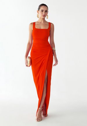 Fel oranje mouwloze jurk met vierkante halslijn, gerimpelde textuur, hoge split aan de linkerkant, gecombineerd met een gouden clutch en sandalen.