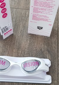 Gafas de natación blancas con un diseño aerodinámico, lentes anti-vaho y texto rosa que dice "MAX VISION". Viene con un estuche resistente.