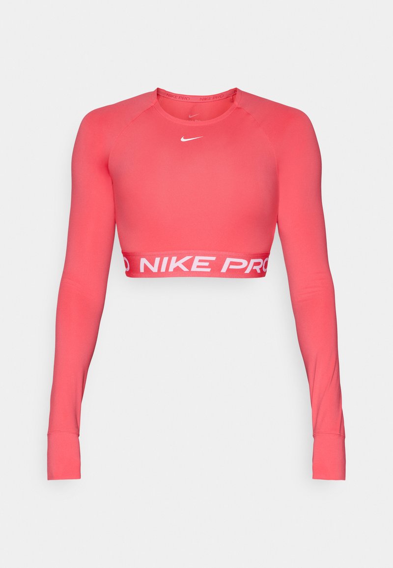 Długi rękaw crop top Nike Pro w jasnym koralowym kolorze, wykonany z elastycznego materiału. Posiada okrągły dekolt i białe logo "NIKE PRO" na dole.