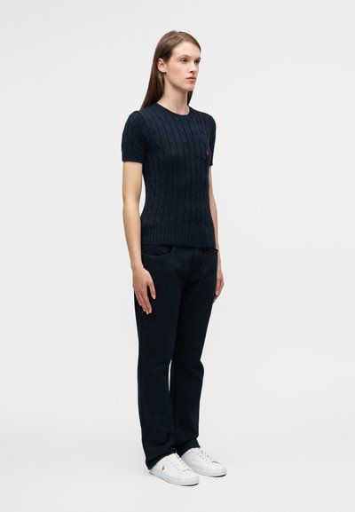 Merensininen neulottu lyhythihainen villapaita, jossa palmikkokuvio, yhdistetty tummiin farkkuihin ja valkoisiin tennareihin. Rintapielessä hillitty punainen logo.