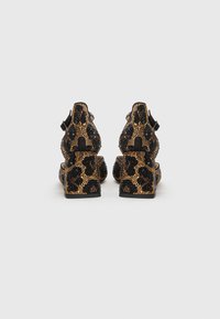 Black and gold embellished heels featuring a leopard pattern, with a block heel and side strap closure. Textured and sparkly finish.