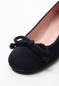 Marinblå mocka ballerina med rund tå, med en knuten repdetalj framtill och en ljusrosa innersula.