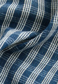 Textil med en strukturerad blå tyg med vita ränder och ett rutmönster, som visar en mjuk, vävd yta.