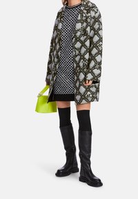 Cappotto grigio a motivo con accenti verdi, abito nero con motivo a cerchi, borsa giallo neon e stivali neri al ginocchio.