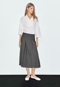 Camicia bianca oversize con colletto pieghettato, abbinata a una gonna grigia plissettata fino al ginocchio e scarpe flat bianche. Tessuto morbido, design minimalista.