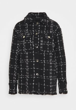 Schwarze knöpfbare Jacke mit weißem Karomuster, zwei Brusttaschen mit Knöpfen, Kragen sowie ausgefranstem Saum und Manschetten.