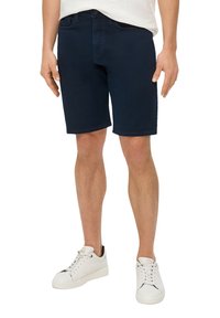 Granatowe szorty dżinsowe o prostym kroju z subtelnymi detalami w stichu, noszone z białymi sneakersami. Zawierają zapięcie na guzik i zamek błyskawiczny.