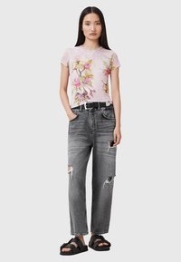 Blomstermønstret lyserød t-shirt med kort ærme, slidte grå jeans, sort bælte og klodsede sorte sandaler. Casual, afslappet pasform.